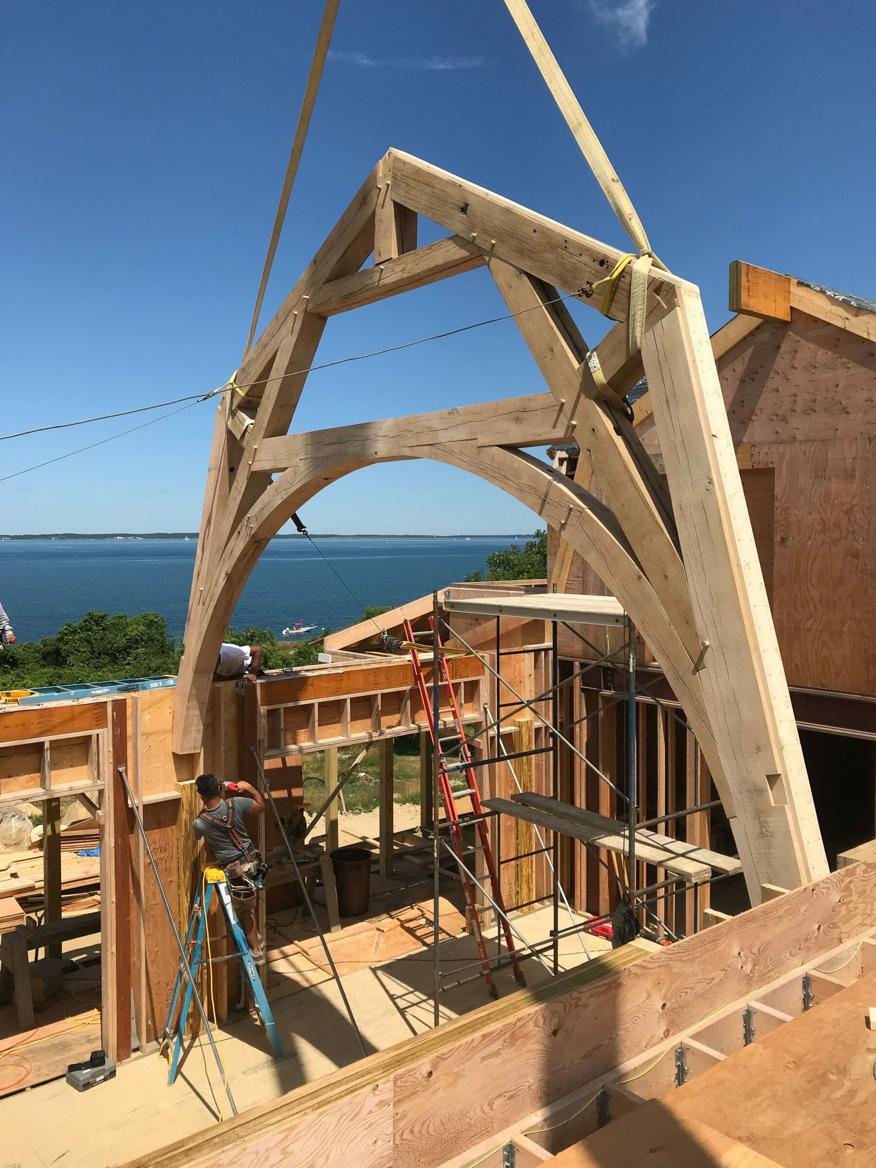 The reclaimed oak hammer beam truss being lowered into place by crane at the Seven Gates Residence in Martha's Vineyard