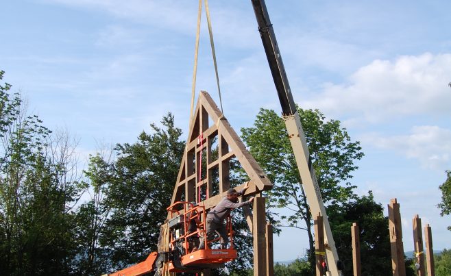 Gable end timber truss being set into place with a crane and a boom lift.