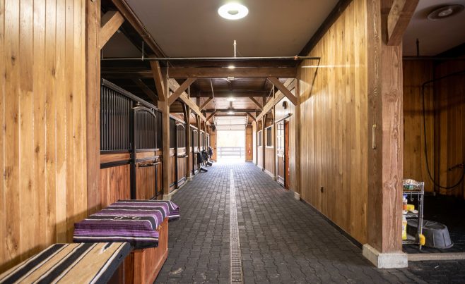 Center aisle of a post and beam horse barn featuring a brick floor.