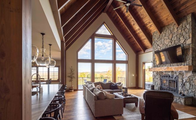 Mountain views from a living room featuring a stone fireplace and post and beam frame.