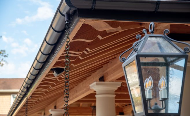 A custom timber framed pavilion with a clay tile roof, outdoor seating, custom lighting, and stone pillars in a Mediterranean style