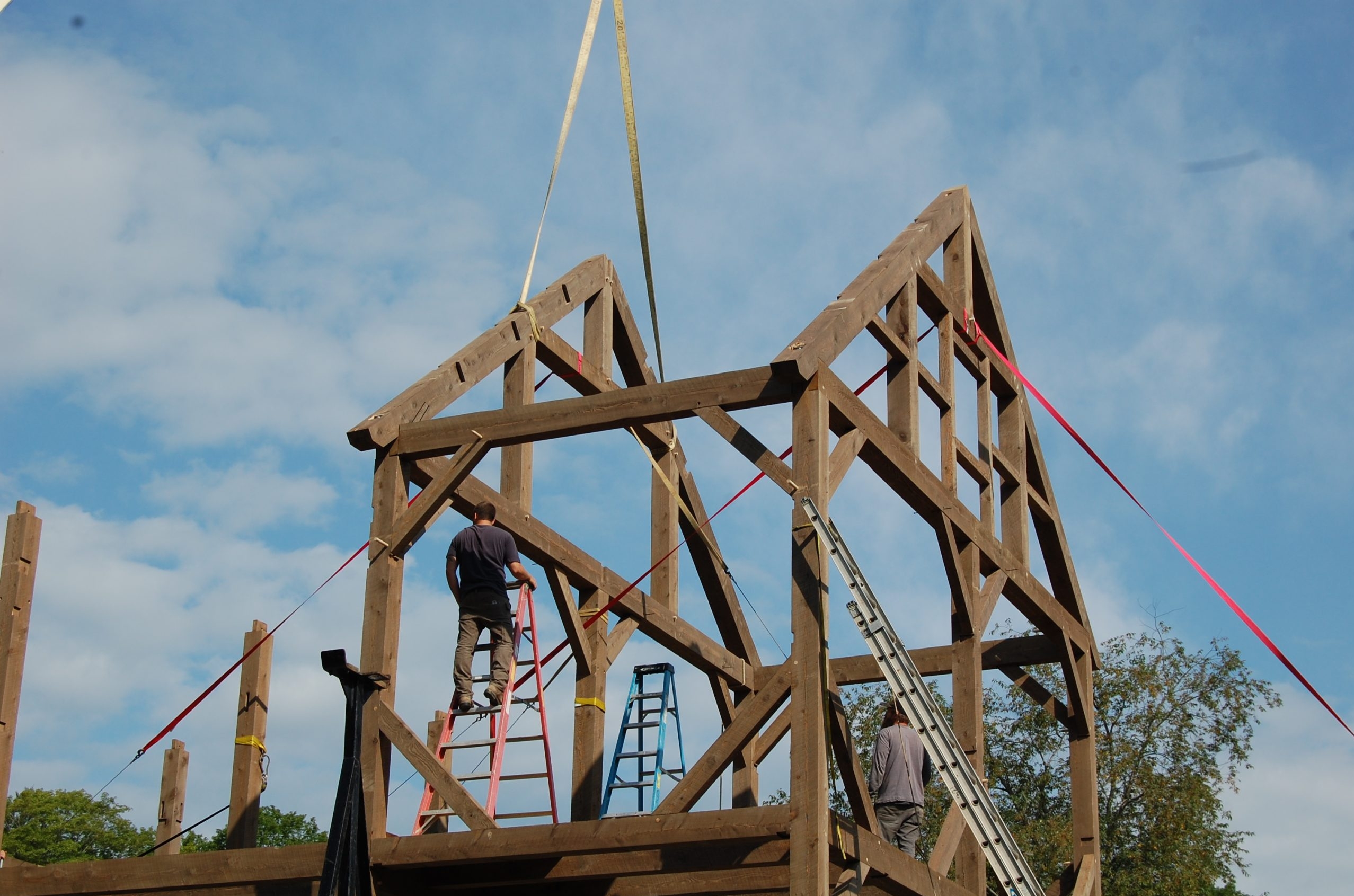 Frame of a wooden house under construction with workers on ladders against a blue sky with red safety lines