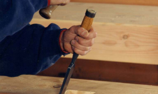 Craftsman's hands hammering a nail into a wooden beam with a hammer in hand